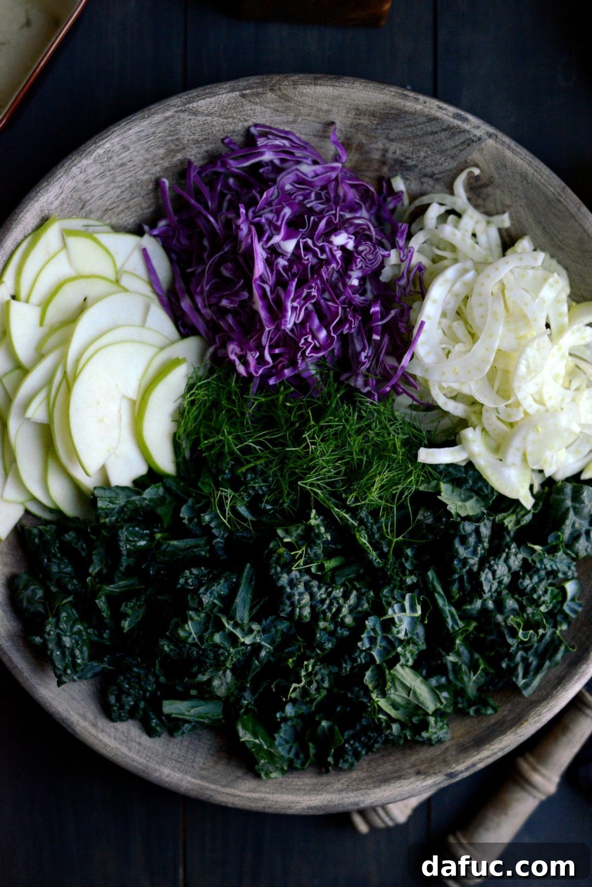 Adding prepped kale, fennel, cabbage, and apple to a large salad bowl.