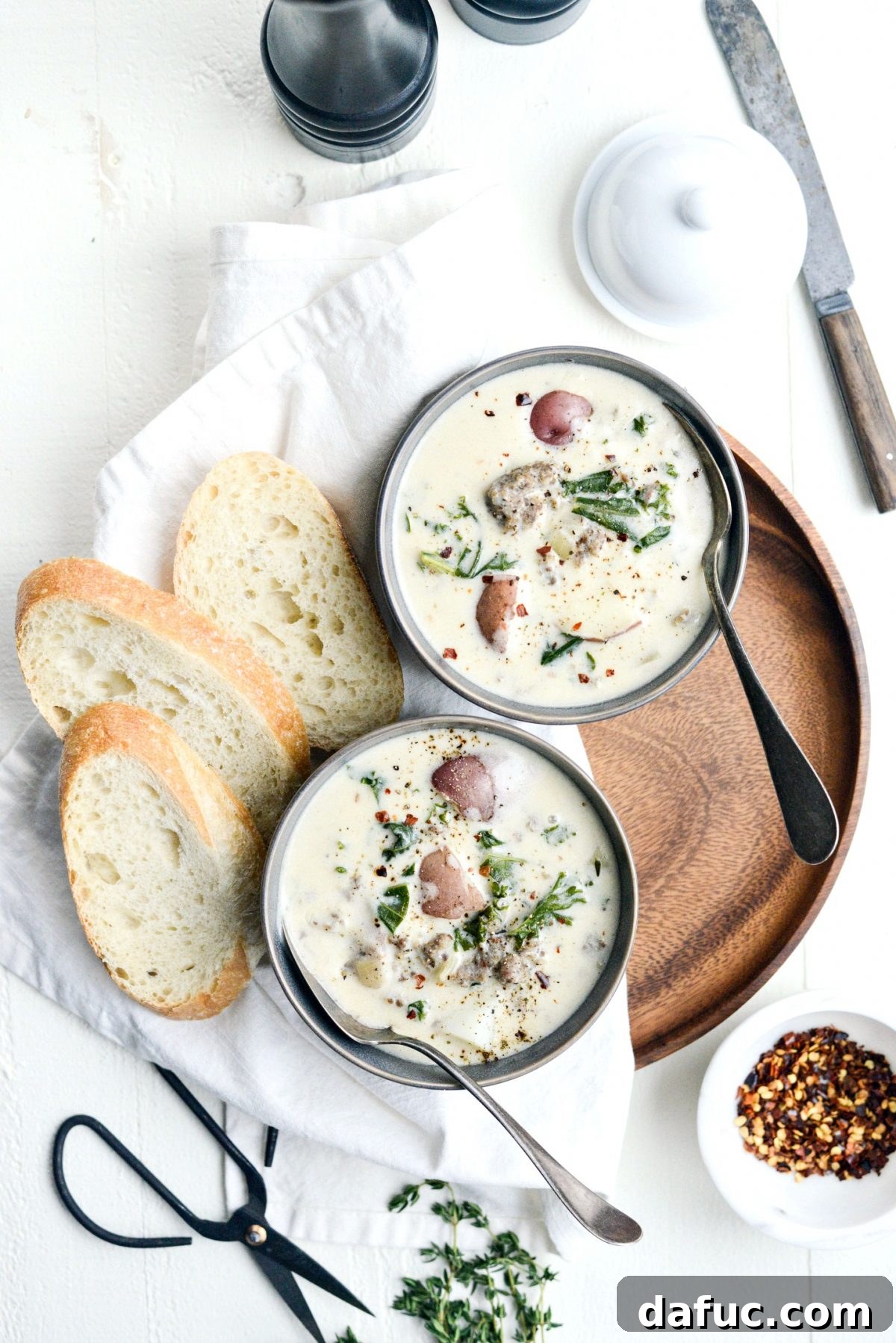 Serving of Creamy Potato, Sausage and Kale Soup garnished with fresh herbs.
