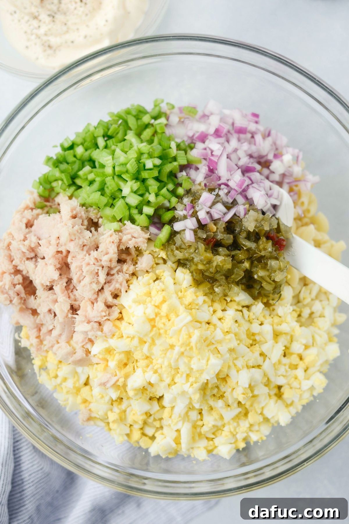 Tossing cooked macaroni with flaked tuna and other ingredients