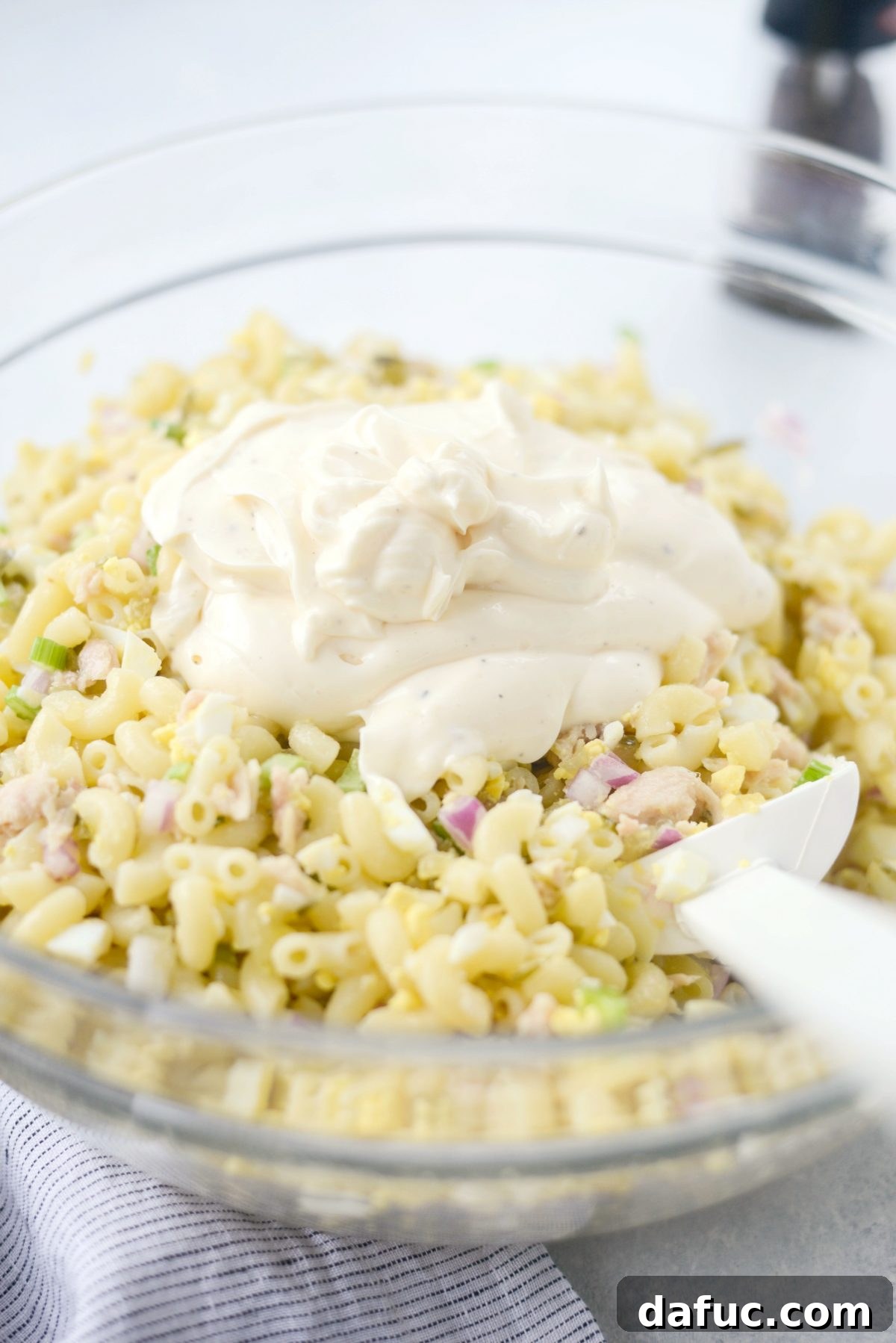 Pouring creamy mayonnaise dressing over the tuna macaroni salad ingredients