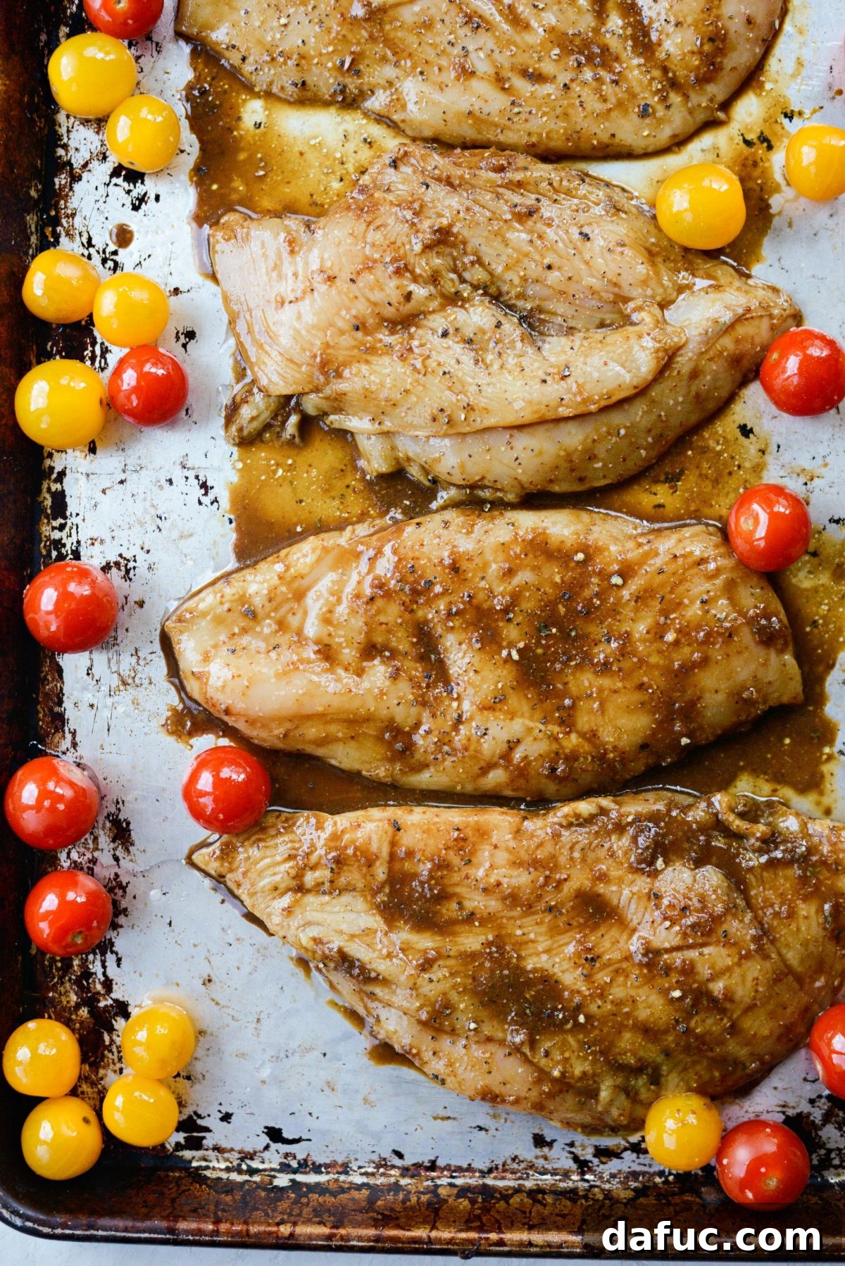 Marinated chicken and seasoned tomatoes arranged on a sheet pan