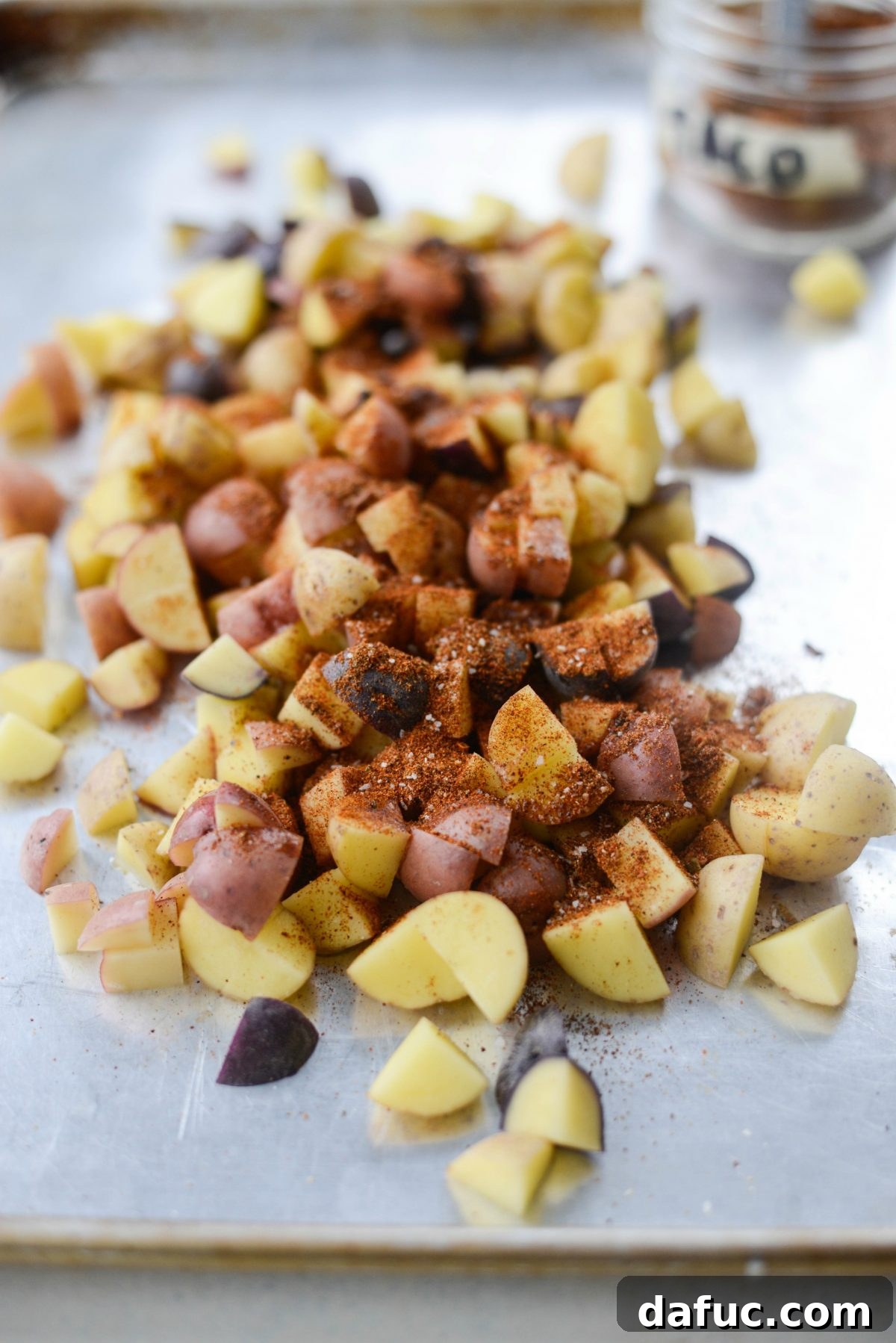 Easy Turkey Taco Breakfast Scramble Meal Prep 5 Diced baby potatoes seasoned with taco seasoning and a dash of cayenne pepper on a metal baking sheet, ready for roasting.