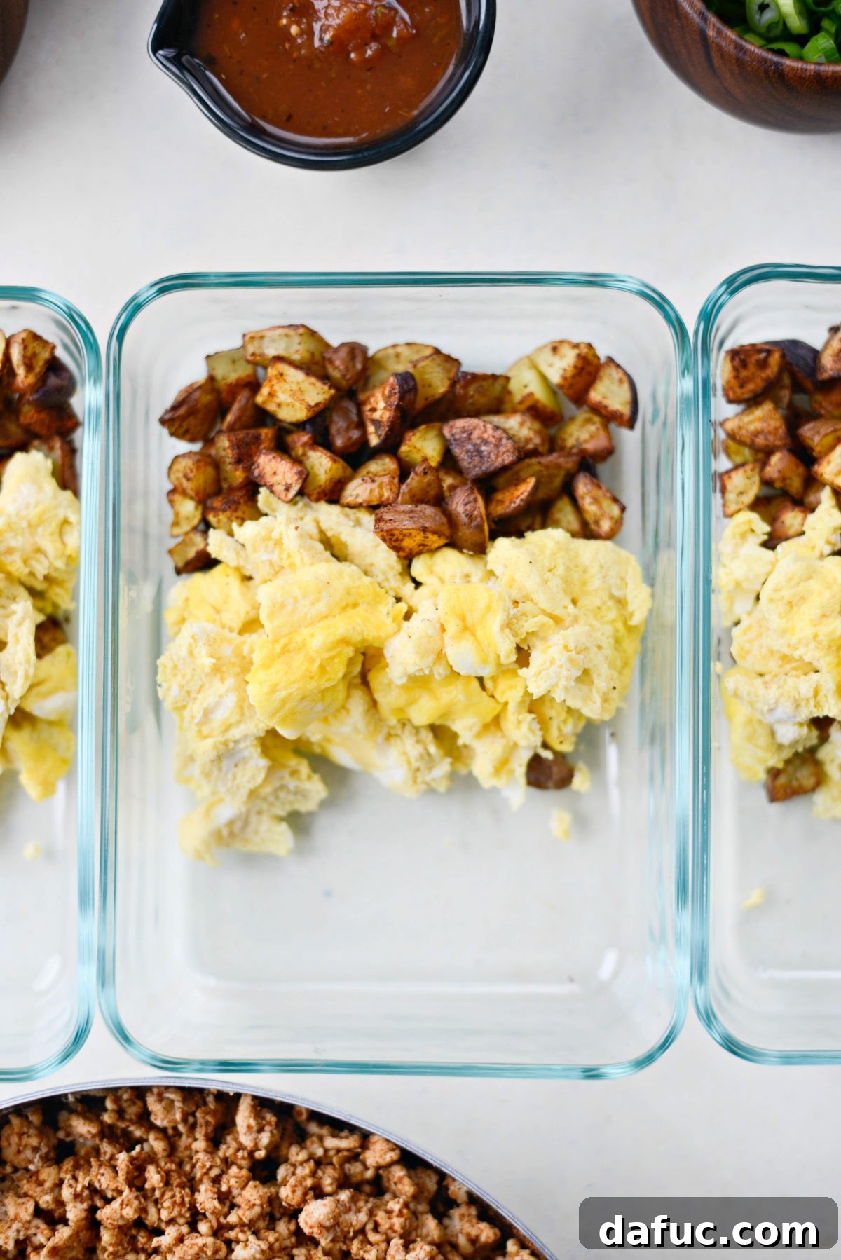 Easy Turkey Taco Breakfast Scramble Meal Prep 8 Assembling meal prep containers with roasted potatoes, scrambled eggs, and turkey taco meat.