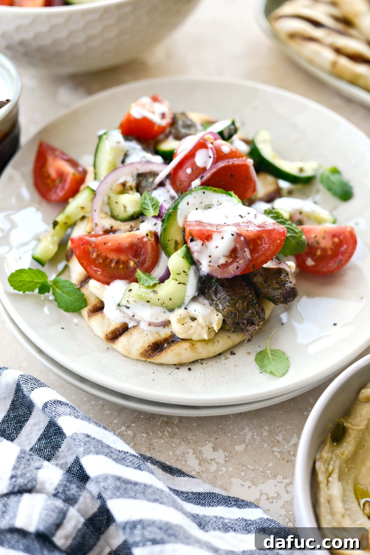 A vibrant Lamb Kofta Open-Faced Pita, loaded with fresh toppings and a drizzle of white sauce