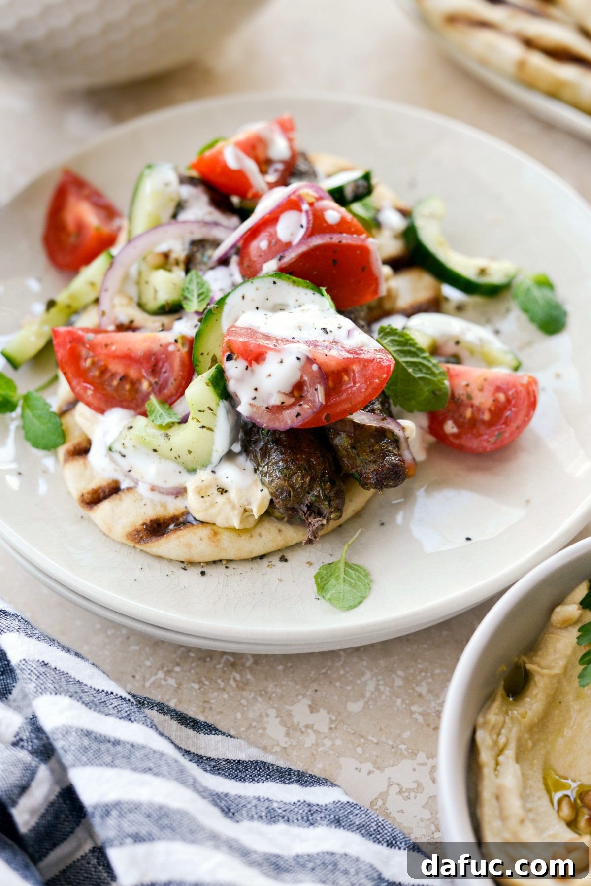 Close-up view of a Lamb Kofta Open-Faced Pita, showcasing toppings and garlic yogurt sauce