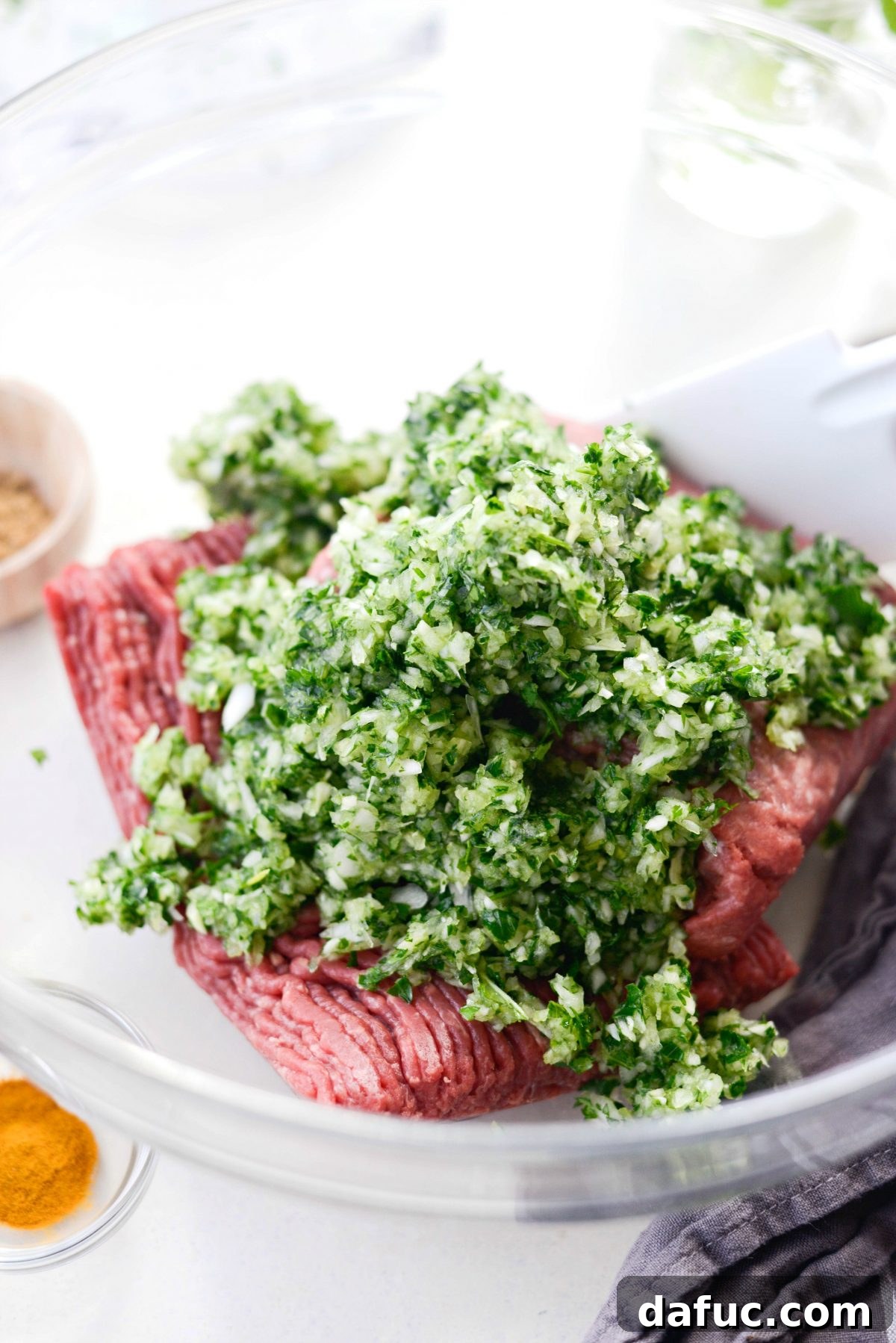 Ground lamb and beef being mixed with the minced herb and onion paste in a large bowl