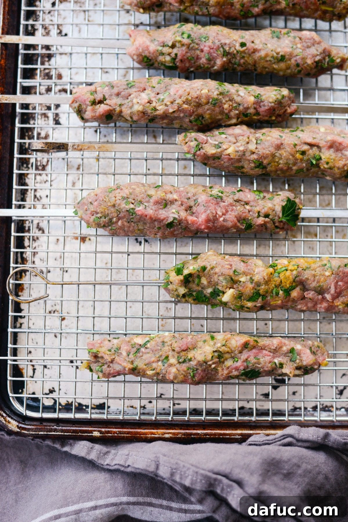Shaping the seasoned lamb and beef mixture around metal skewers for baking