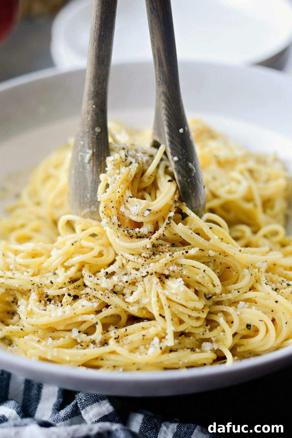 Reimagined Cacio e Pepe Carbonara 12 A close-up shot of Cacio e Pepe Carbonara being served with wooden spoons, highlighting its textures.