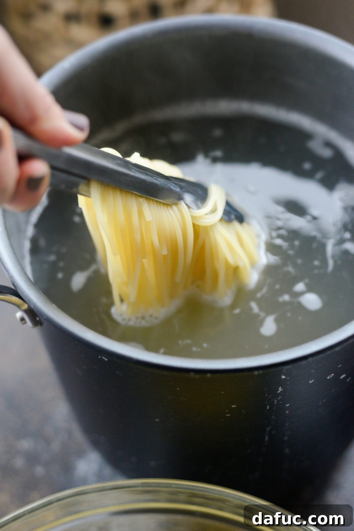 Removing hot cooked spaghetti from the pot directly into the prepared egg and cheese mixture using tongs.