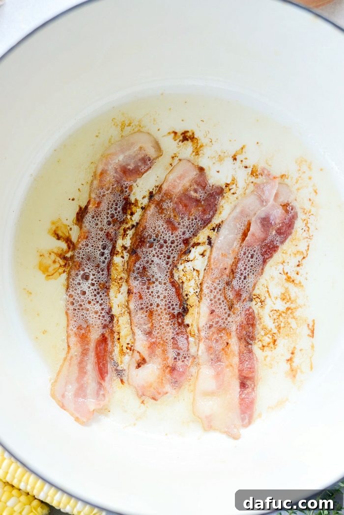 Golden Harvest Corn and Zucchini Chowder 5 A close-up of thinly sliced bacon being cooked in a Dutch oven, sizzling to a perfect crisp, setting the foundation for the chowder.