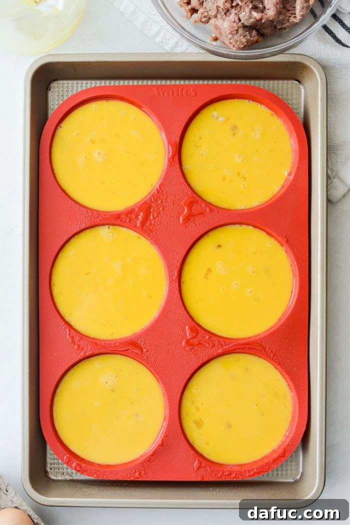 Hearty Sausage Egg and Cheese Breakfast Melts 8 Pouring whisked eggs into the prepared silicone mold