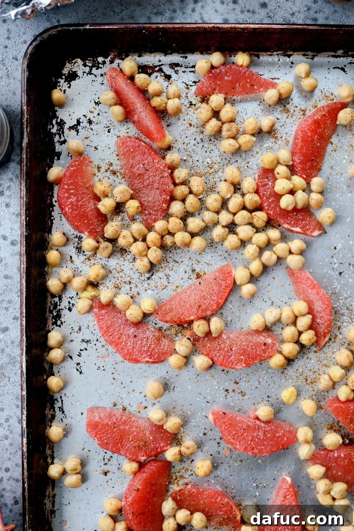 Roasted grapefruit segments and chickpeas on a baking sheet, seasoned with spices.