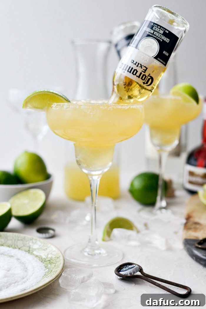 Signature Beergarita 2 Two refreshing Beergaritas served in salt-rimmed glasses with inverted Coronita bottles, garnished with lime wedges.