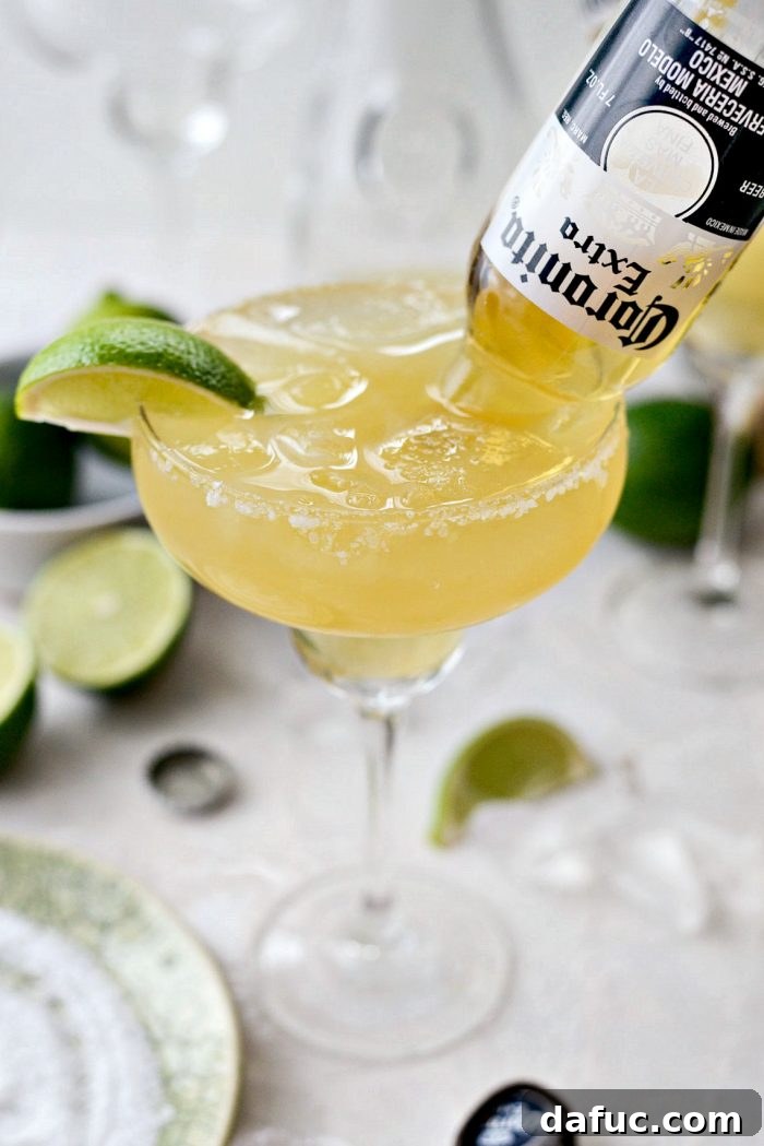 Signature Beergarita 3 Close-up of a Beergarita cocktail in a salt-rimmed glass, featuring an inverted Coronita beer bottle and a lime wedge garnish.