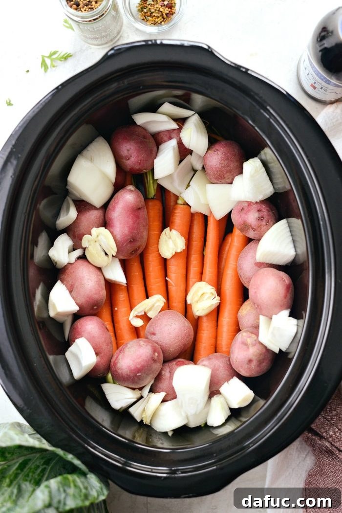 Effortless Slow Cooker Corned Beef and Cabbage 5 Raw carrots, potatoes, onion, and garlic in the bottom of a slow cooker