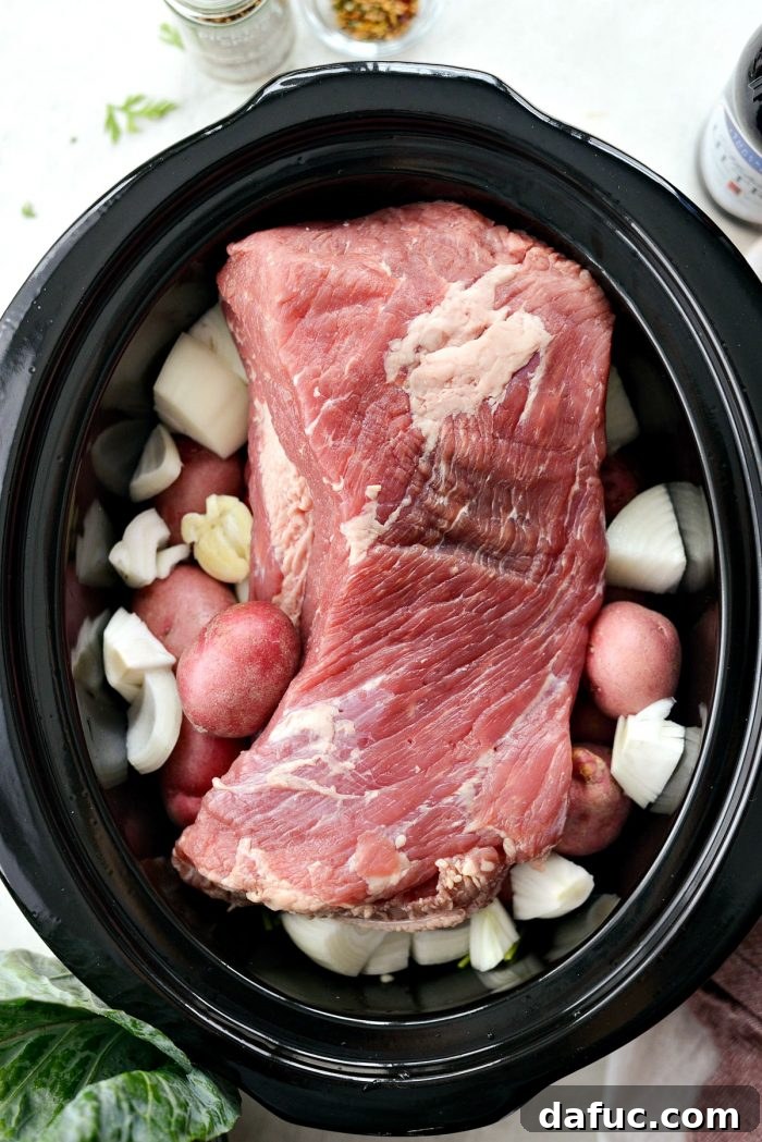 Effortless Slow Cooker Corned Beef and Cabbage 6 Corned beef brisket being placed on top of vegetables in a slow cooker
