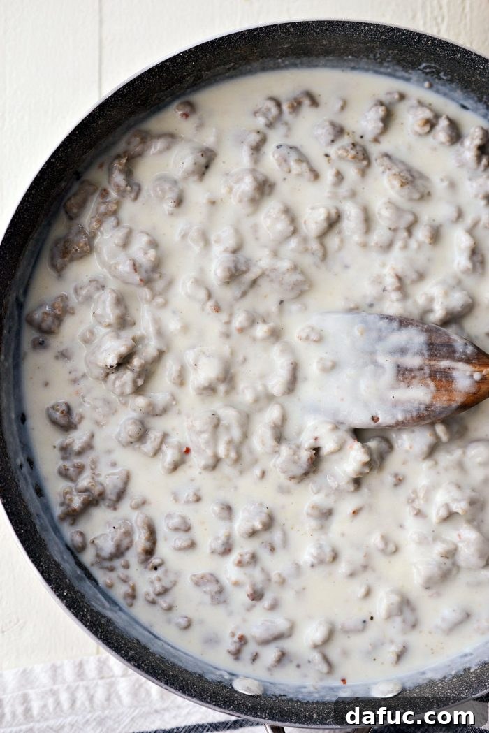Turkey sausage gravy simmering in a skillet, visibly thickening to a creamy consistency.