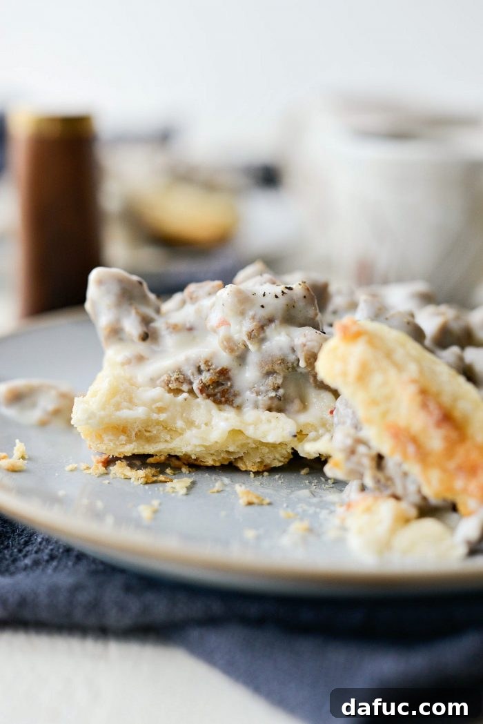Fluffy Greek yogurt biscuits split open and covered with generous spoonfuls of homemade Turkey Sausage Breakfast Gravy, garnished with black pepper.