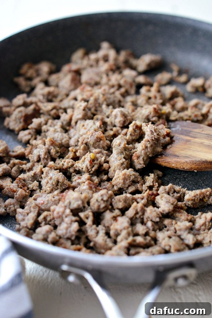 Ground turkey sausage being broken up with a wooden spatula in a hot skillet, ensuring even cooking and browning.