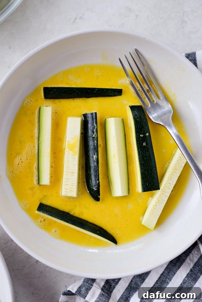 Crispy Air-Fried Zucchini Sticks 12 Zucchini fries dipped in beaten egg, ready for breading.