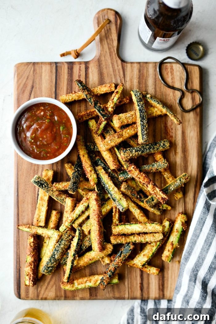 Crispy Air-Fried Zucchini Sticks 23 Air Fryer Zucchini Fries served on a wooden cutting board with basil ketchup and a beverage.