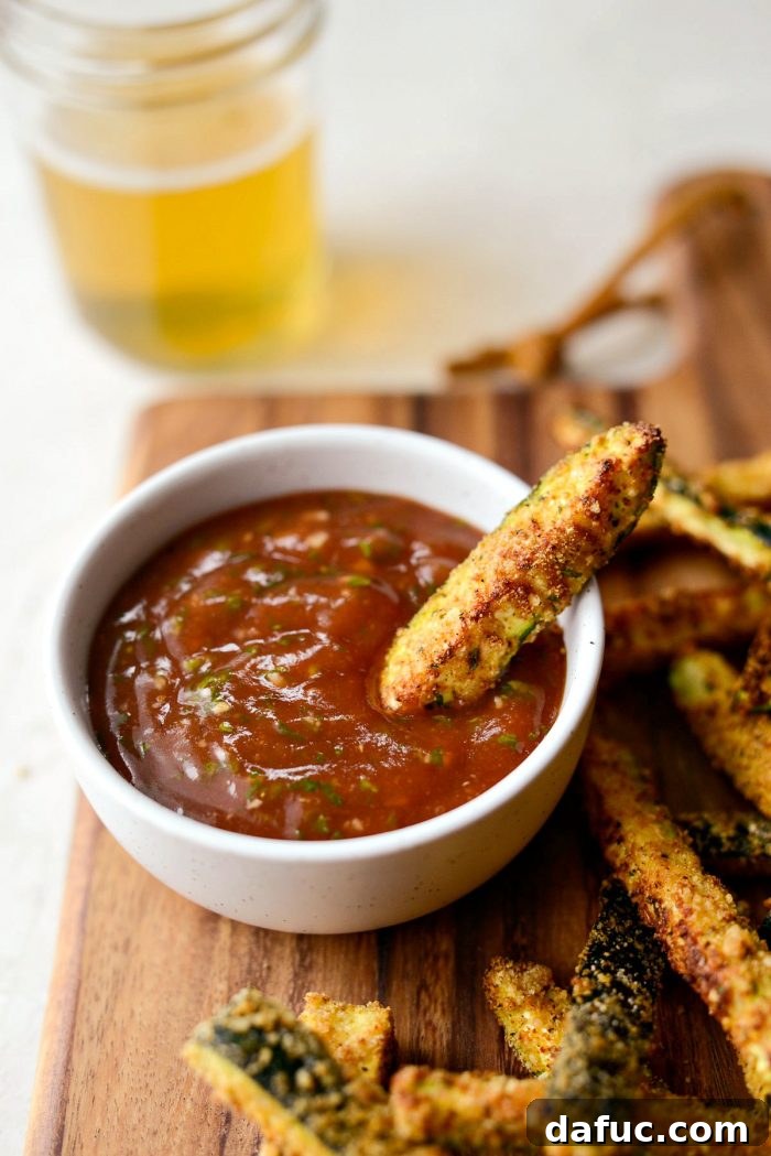 Crispy Air-Fried Zucchini Sticks 24 Close-up shot of a single crispy air-fried zucchini fry being dipped into basil ketchup.