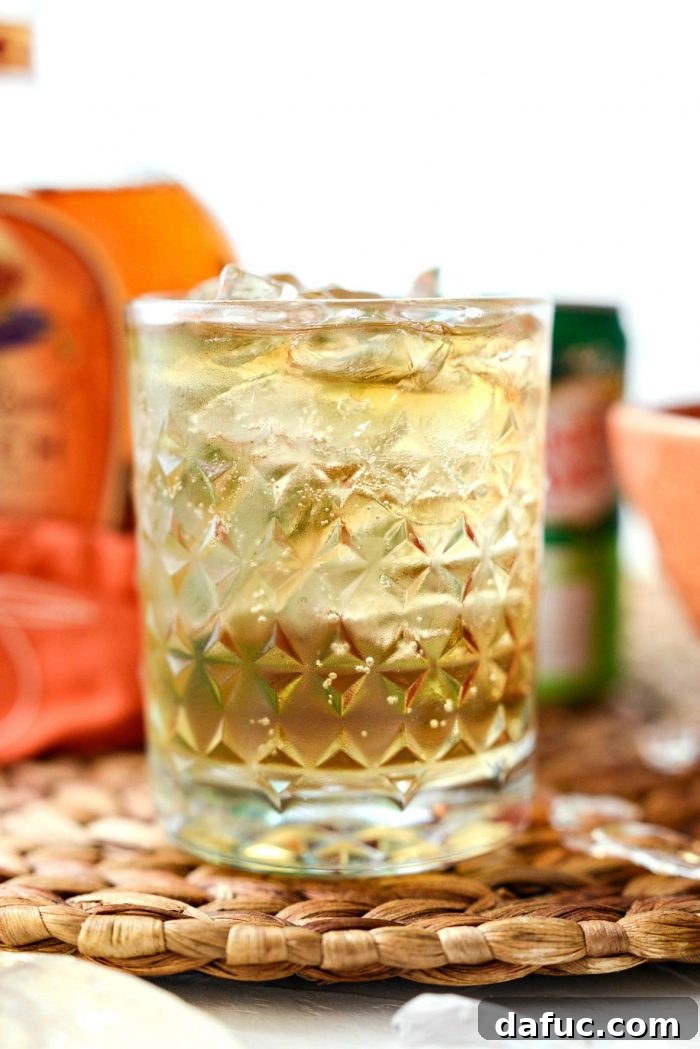 Lewis Peach Ginger Whiskey Infusion 2 Clear textured glass filled with Lewis' Ginger Peach Whiskey Cocktail, garnished with a peach slice.