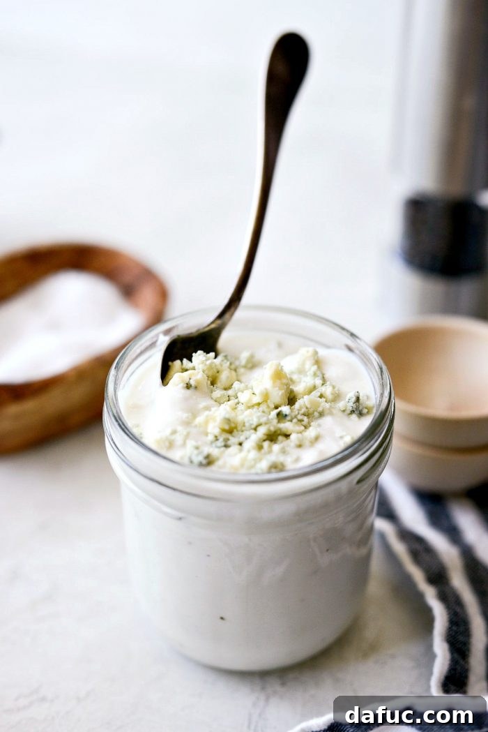 Tangy Greek Yogurt Blue Cheese Dressing 3 Spoon dipping into a jar of homemade Greek Yogurt Blue Cheese Dressing