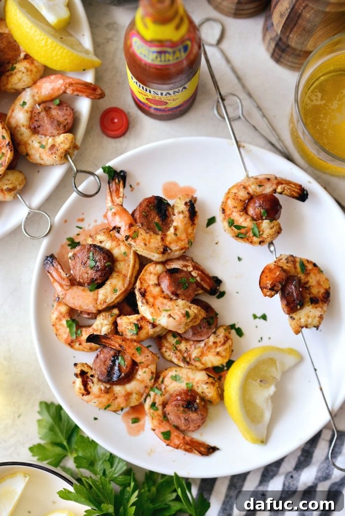 Grilled Cajun Shrimp and Andouille Skewers on a white plate, served with a side of hot sauce for an extra kick.