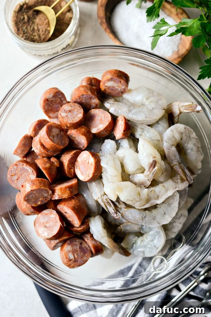 Close-up of jumbo shrimp and sliced chicken andouille sausage in a glass mixing bowl, ready for seasoning.