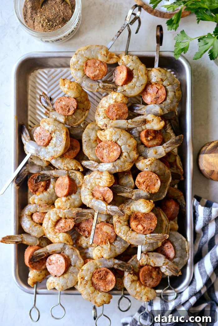 Prepared shrimp and andouille sausage threaded onto metal skewers, ready for grilling.