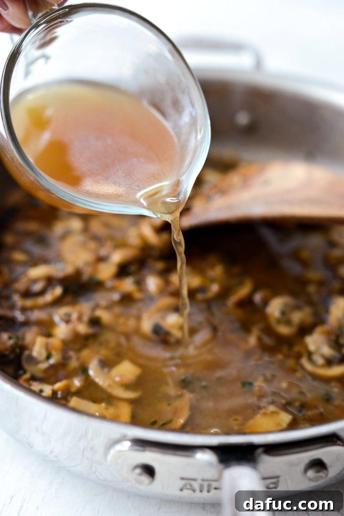 Unsalted chicken stock being added to the skillet, joining the Marsala wine and mushroom mixture.