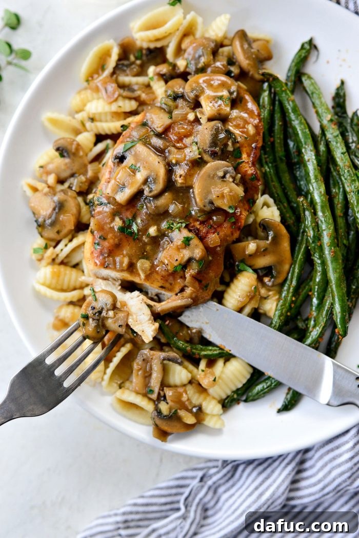 A close-up shot of a perfectly cut piece of Lighter Chicken Marsala, showing the tender chicken and a savory mushroom piece coated in sauce.