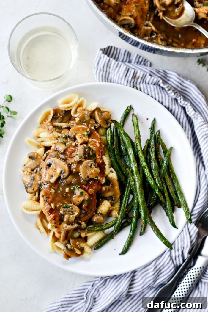 Lighter Chicken Marsala plated elegantly with a generous serving of pasta and vibrant green beans on a white plate, showcasing the rich sauce.