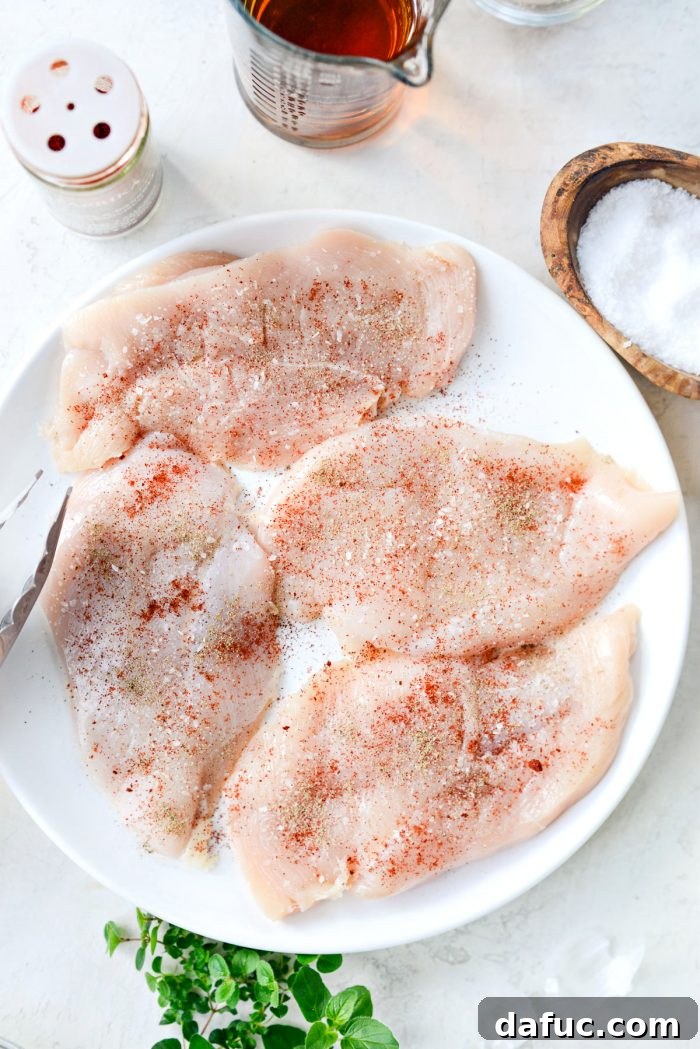 Thin-cut chicken breasts uniformly seasoned with kosher salt, freshly ground black pepper, and paprika, arranged on a white plate.