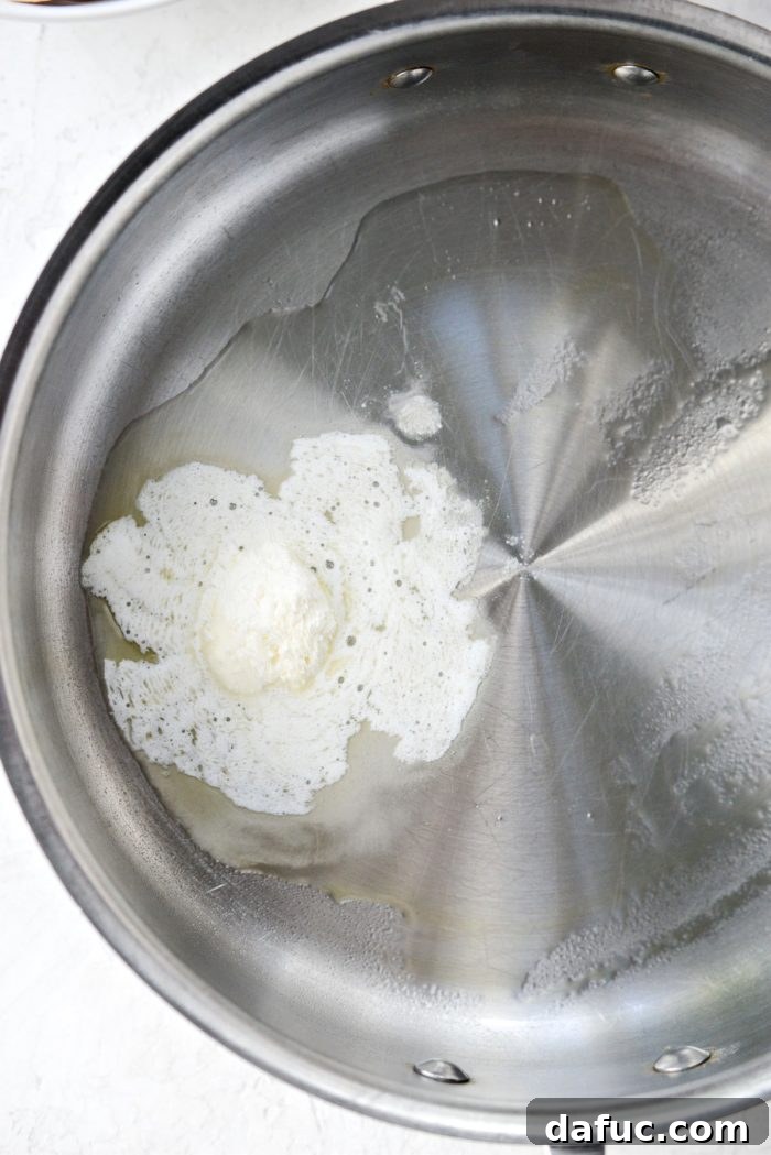 A stainless steel skillet heating on the stovetop, containing a melted mixture of whipped butter and extra light olive oil.