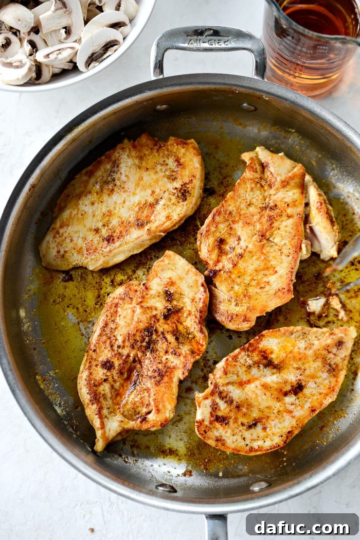 Two pieces of seasoned chicken breast searing to a golden brown in a hot skillet with melted butter and oil.