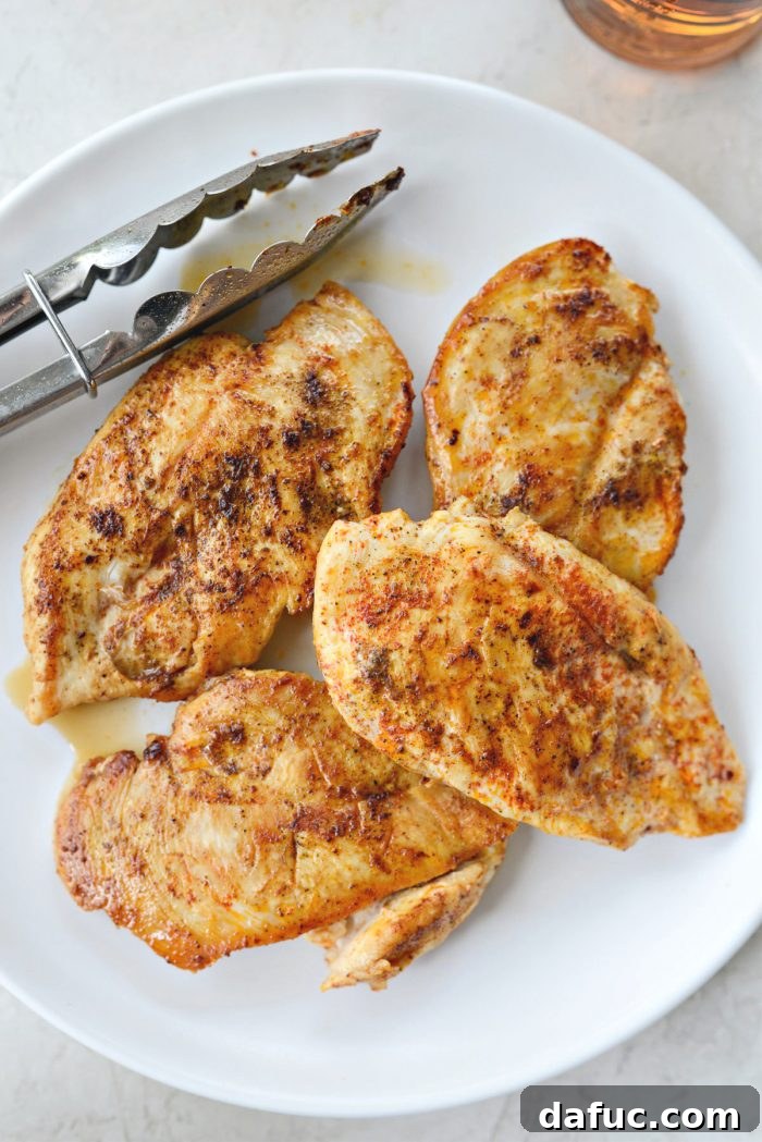 Cooked chicken breasts resting on a clean white plate after being seared in the skillet.