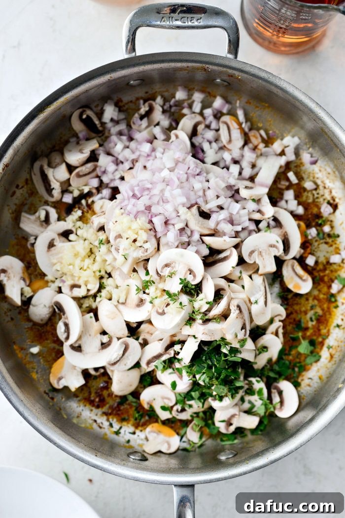 Sliced button mushrooms, minced shallot, chopped garlic, and fresh oregano and thyme leaves added to the skillet.