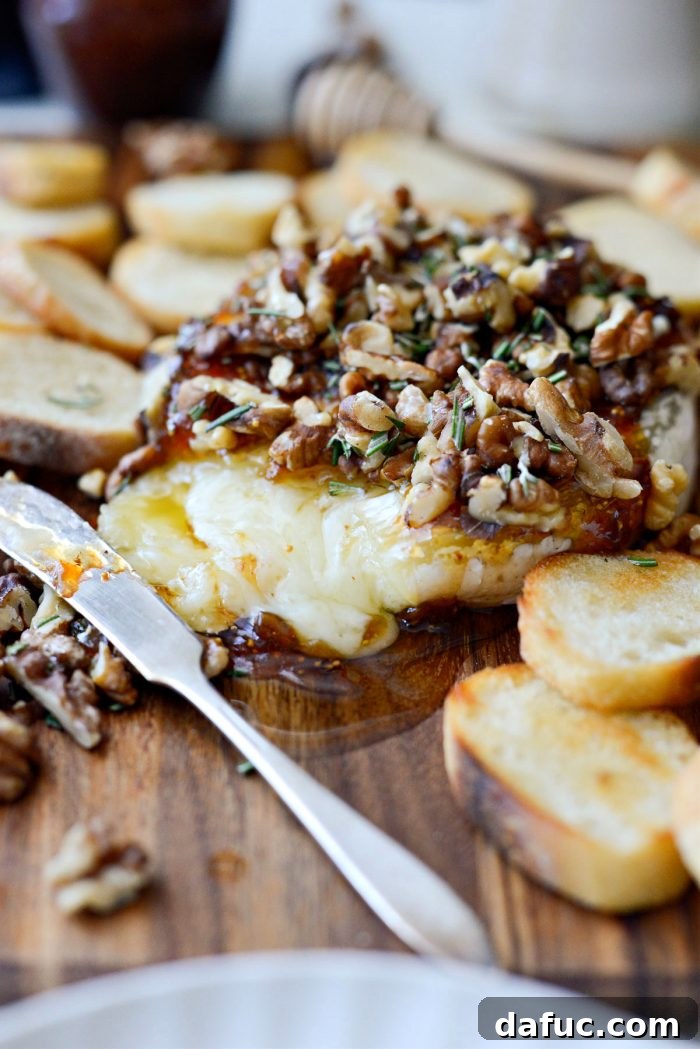 A knife cutting into warm, gooey Honey Baked Brie with fig jam and walnuts.