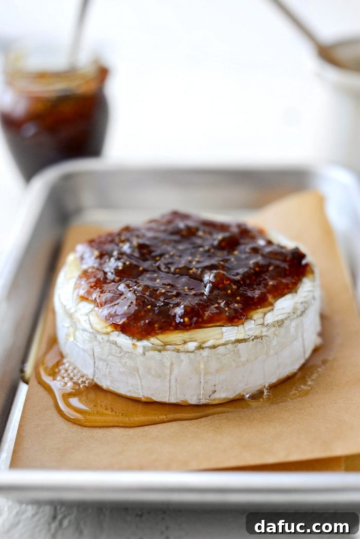 Warm baked brie being topped with spoonfuls of fig jam.
