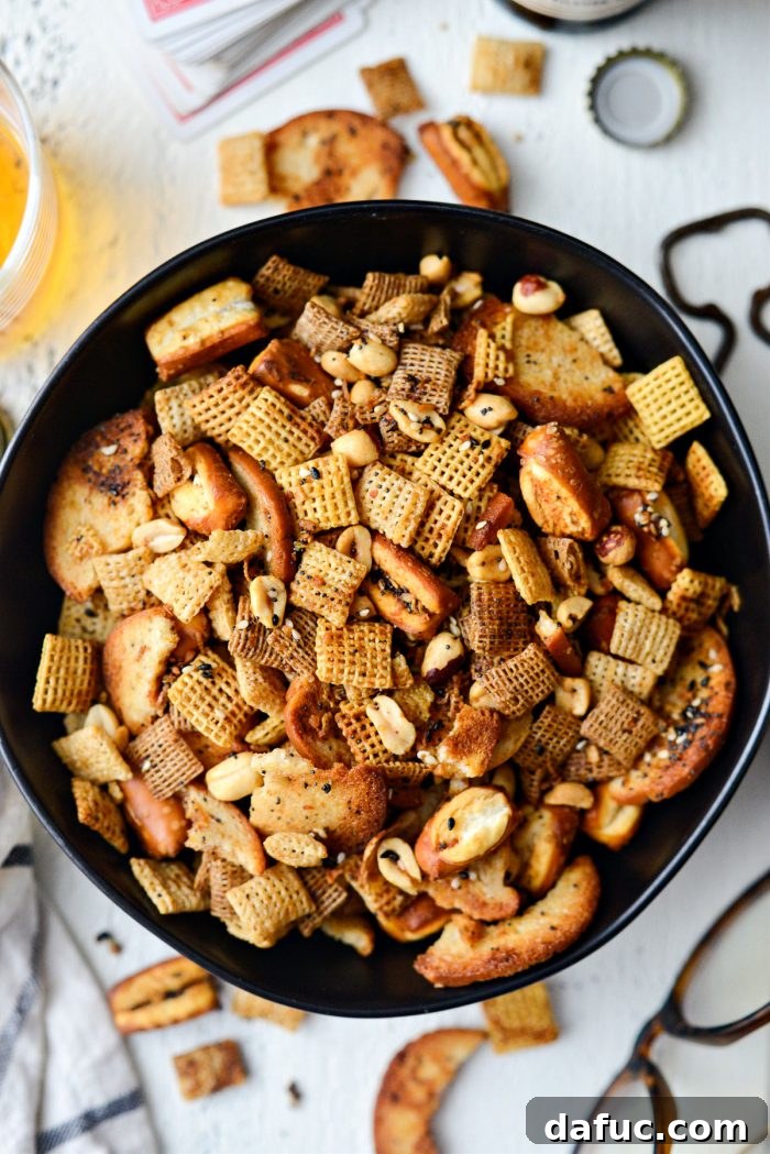 The Ultimate Everything Bagel Chex Mix 2 Delicious Everything Plus the Bagel Chex Mix spread out on a baking sheet, showcasing golden brown cereals, pretzels, bagel chips, and peanuts coated in savory seasoning.