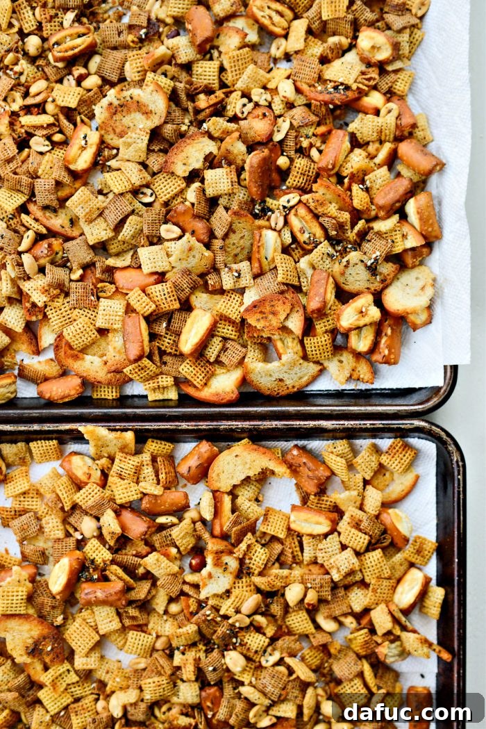 The Ultimate Everything Bagel Chex Mix 11 Freshly baked Everything Plus the Bagel Chex Mix spread out on paper towel-lined baking sheets to cool completely, showcasing its golden brown color and varied textures.