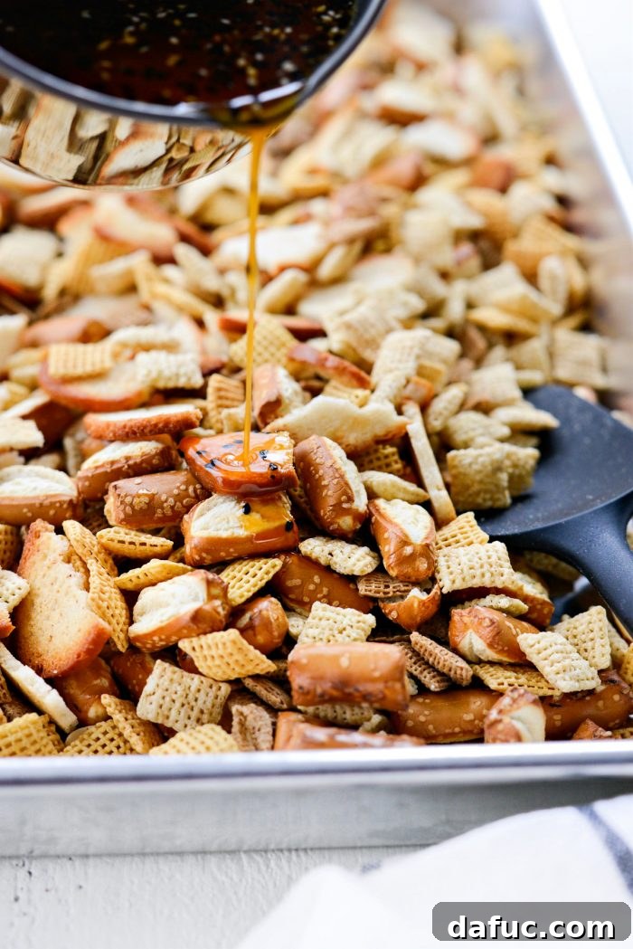 The Ultimate Everything Bagel Chex Mix 8 The savory butter and seasoning mixture being poured evenly over the combined dry ingredients of Chex Mix in a large pan.