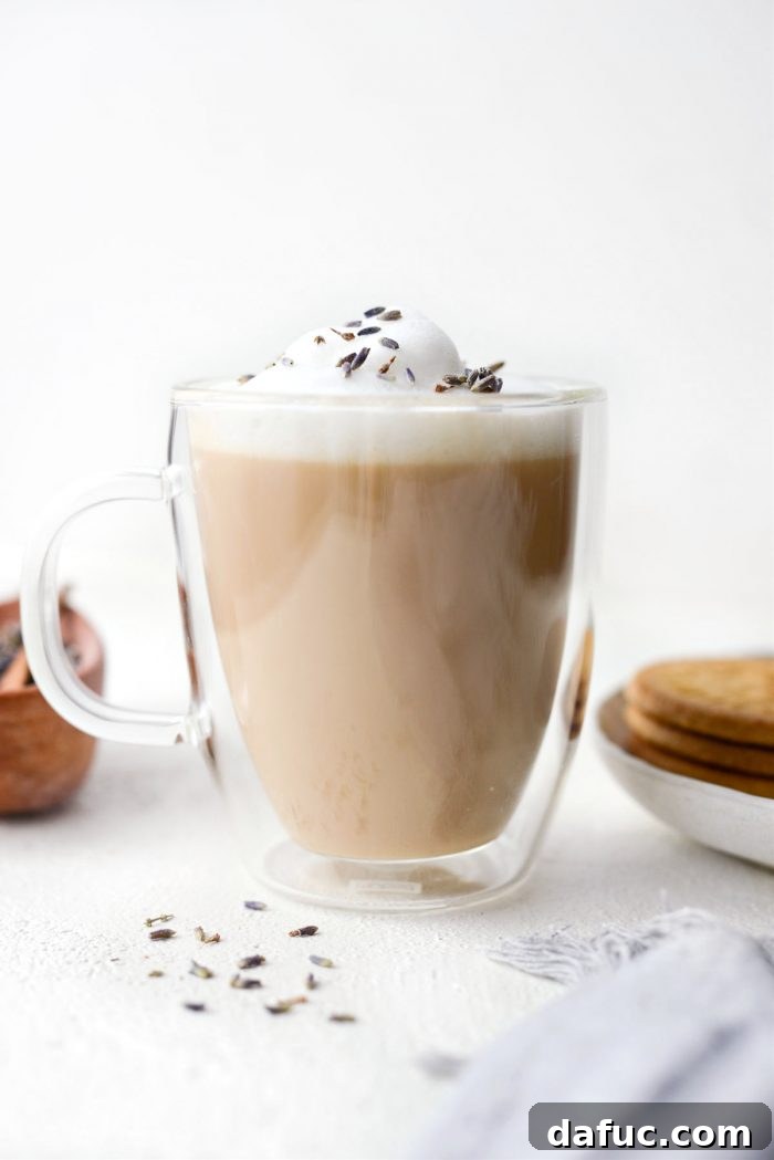 A beautifully prepared London Fog Tea Latte in a clear mug, showcasing layers of tea and frothy milk, with dried lavender blossoms scattered nearby.