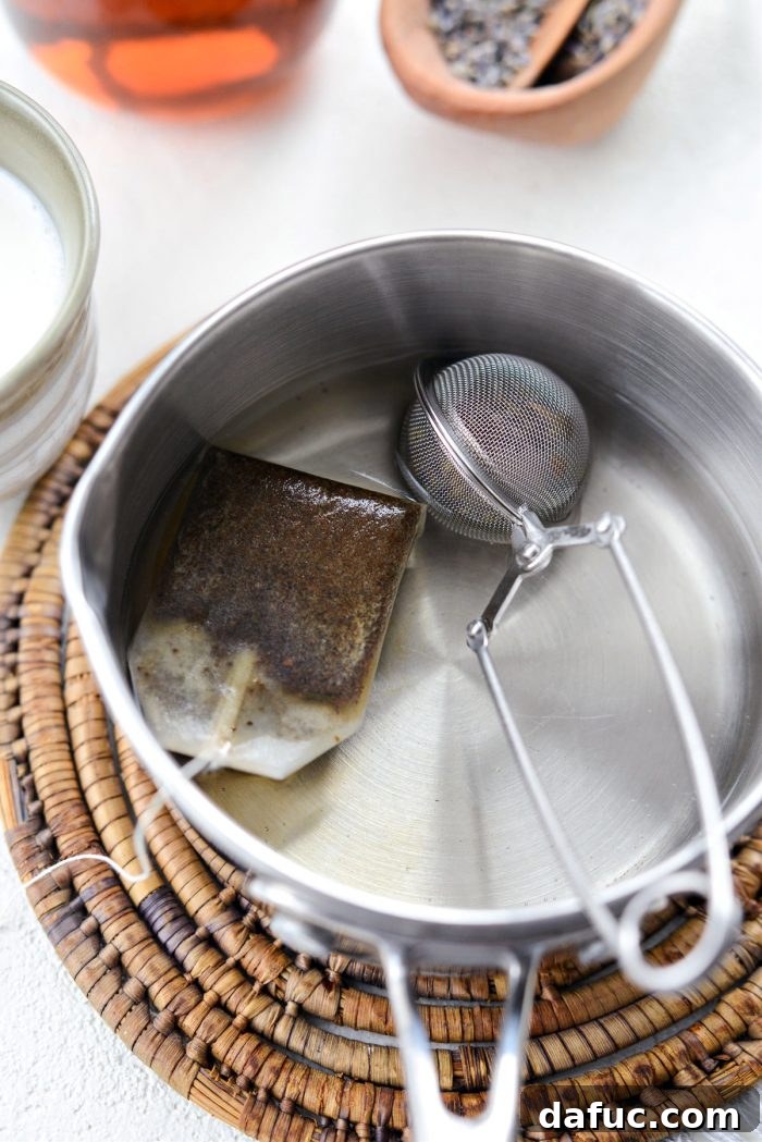 Earl Grey tea bag and lavender infuser steeping in hot water in a saucepan.