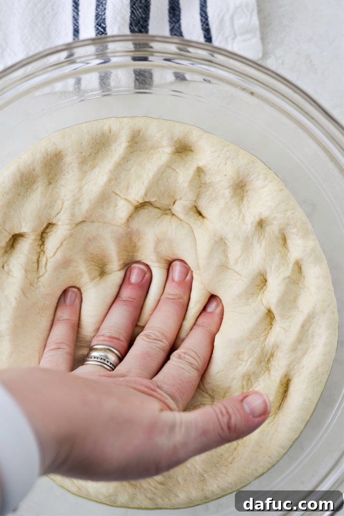 Ultimate Focaccia Pizza 18 Gently pressing down on the risen focaccia dough to deflate it.