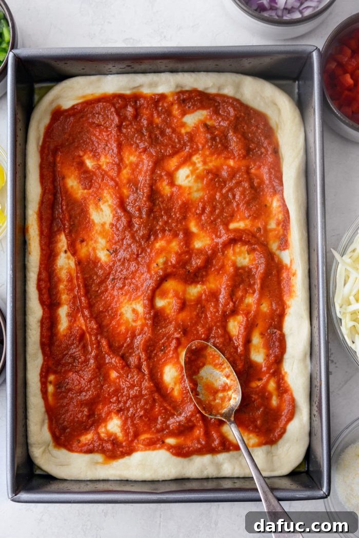 Ultimate Focaccia Pizza 22 Spreading pizza sauce over the dimpled focaccia dough.
