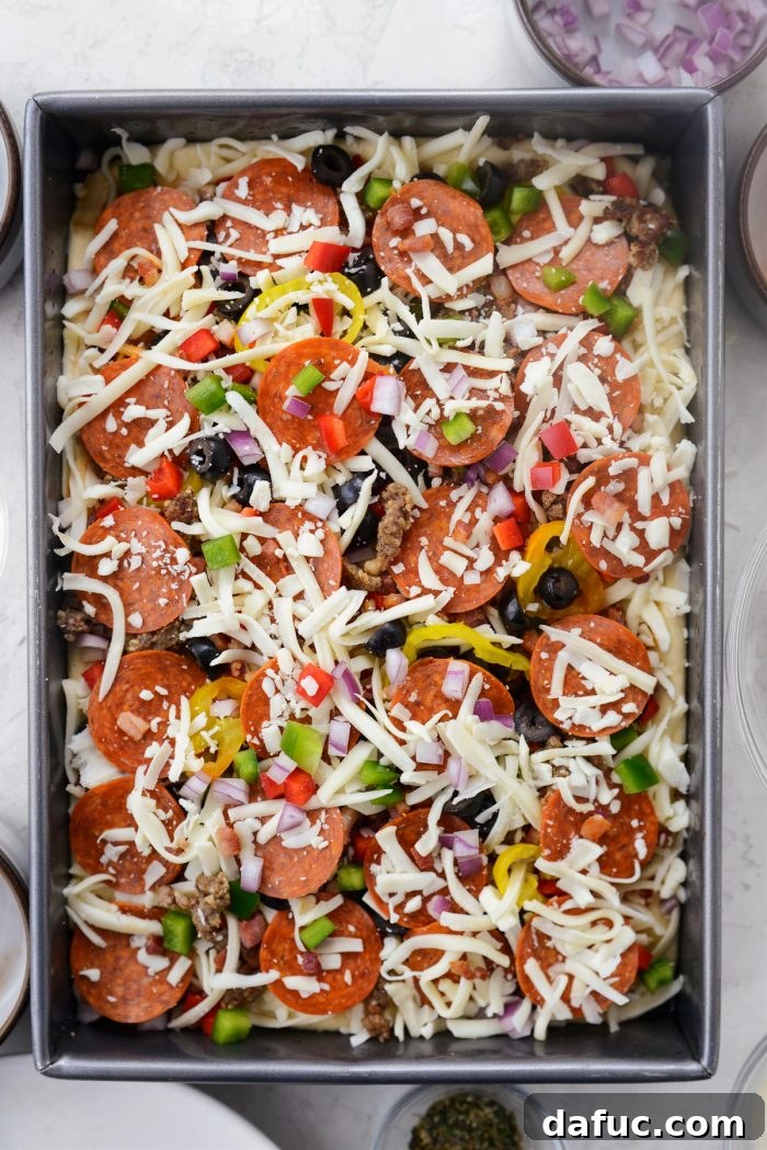 Ultimate Focaccia Pizza 24 Arranging the various toppings, including vegetables and cooked meats, on the pizza.