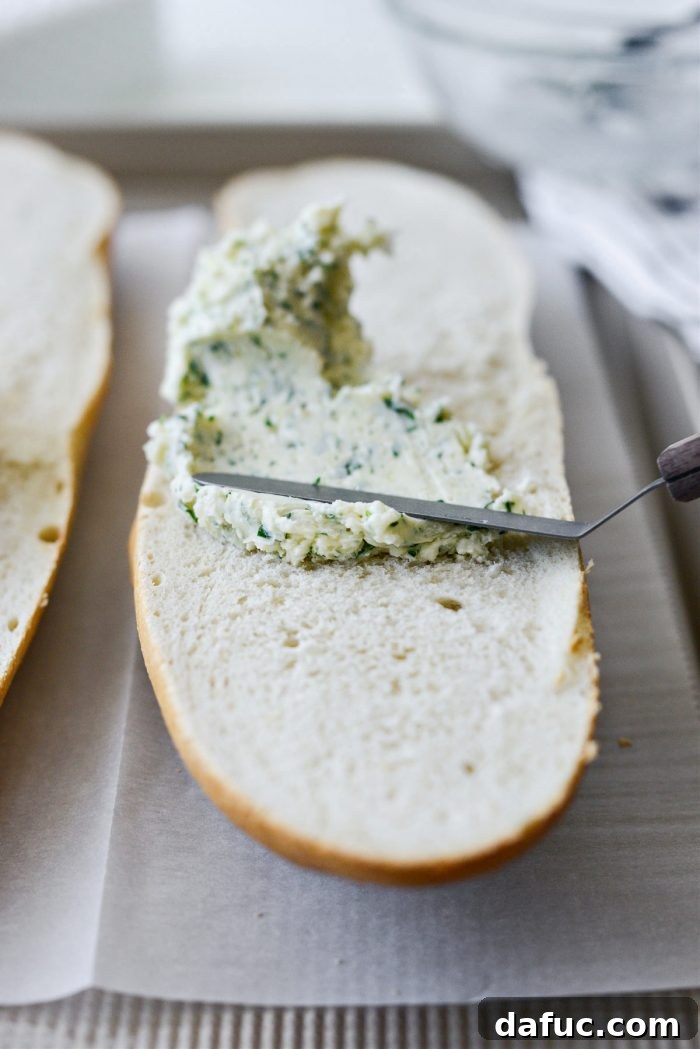 Garlic butter being evenly spread across one half of the sliced bread with a spatula
